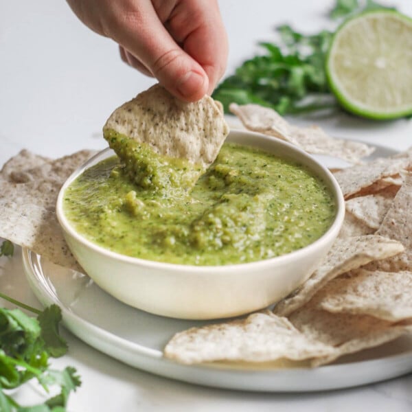 Dipping a tortilla chip into Salsa Verde in a bowl.