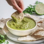 Dipping a tortilla chip into Green Salsa Verde in a bowl.