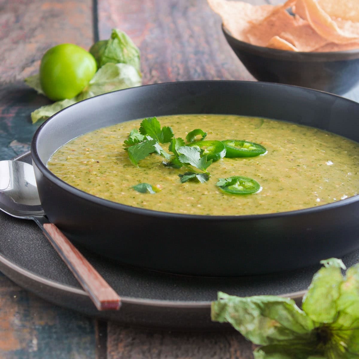 Green Salsa Verde in a black bowl garnished with sliced jalapeno and cilantro.