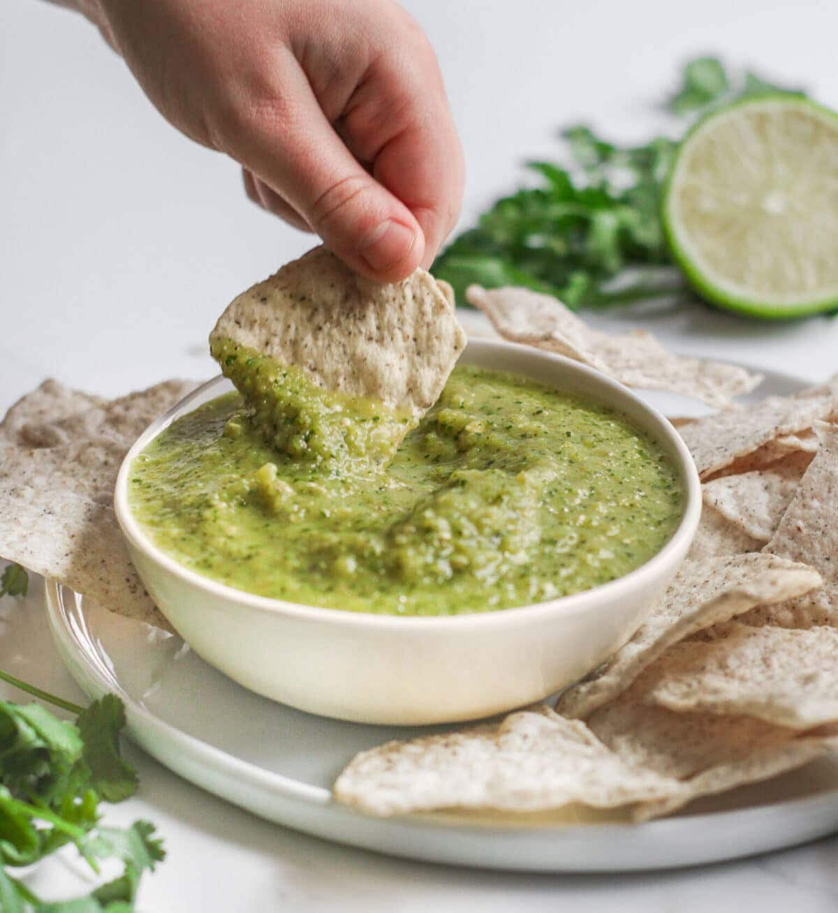Dipping a tortilla chip into Green Salsa Verde in a bowl.