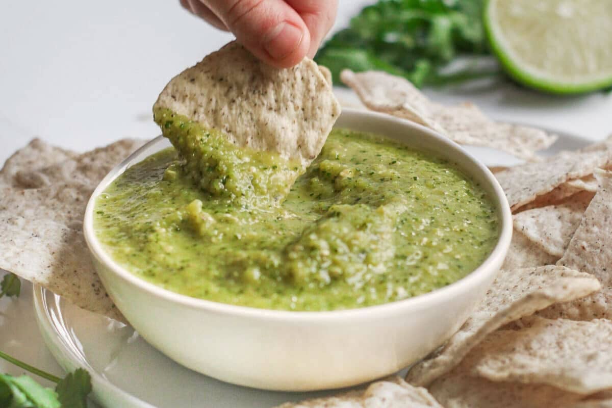Dipping a tortilla chip into Tomatillo Salsa Verde in a bowl.